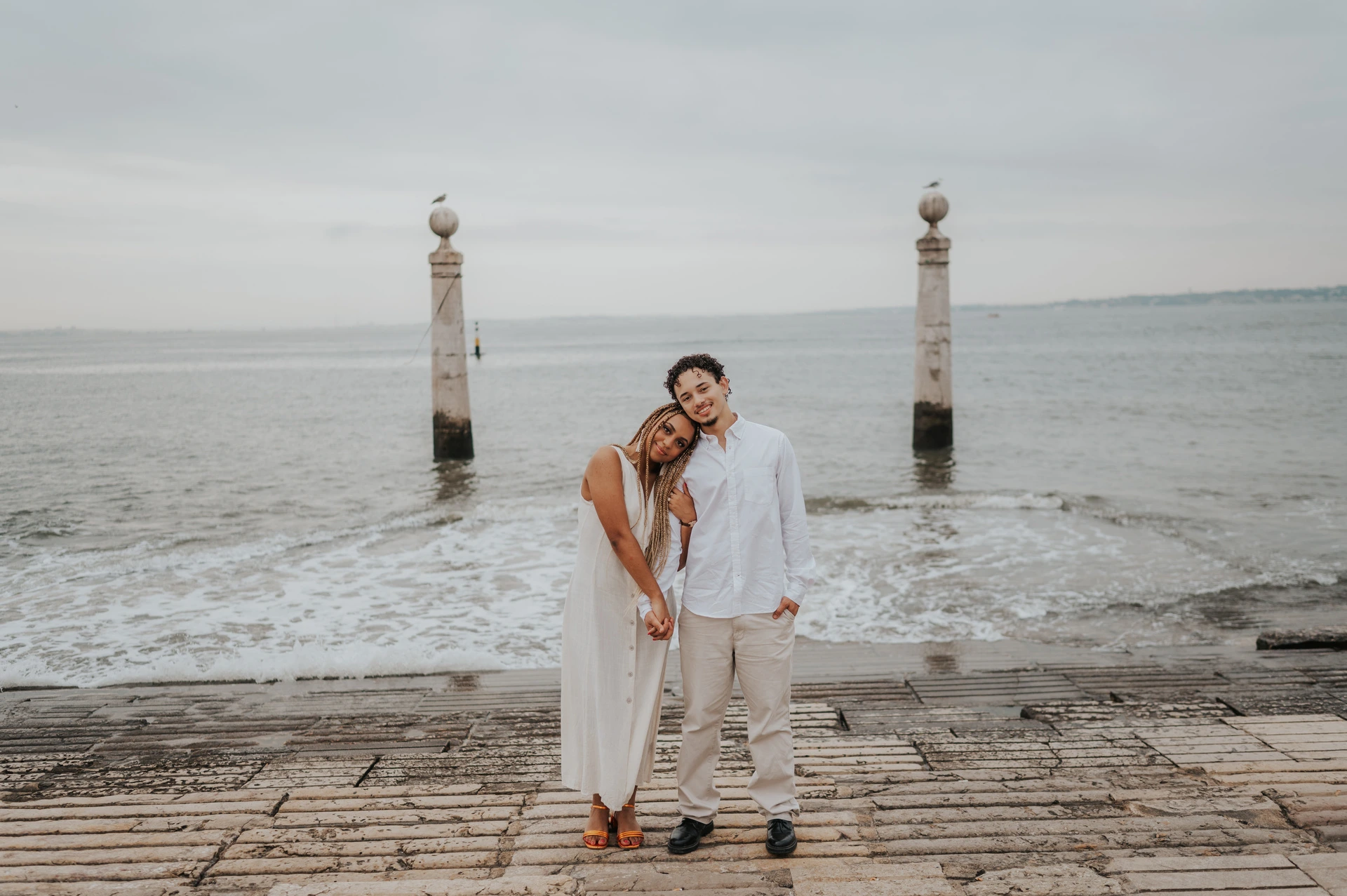 The couple leaning their heads together while standing on the waterfront steps during their couple photoshoot in Lisbon.