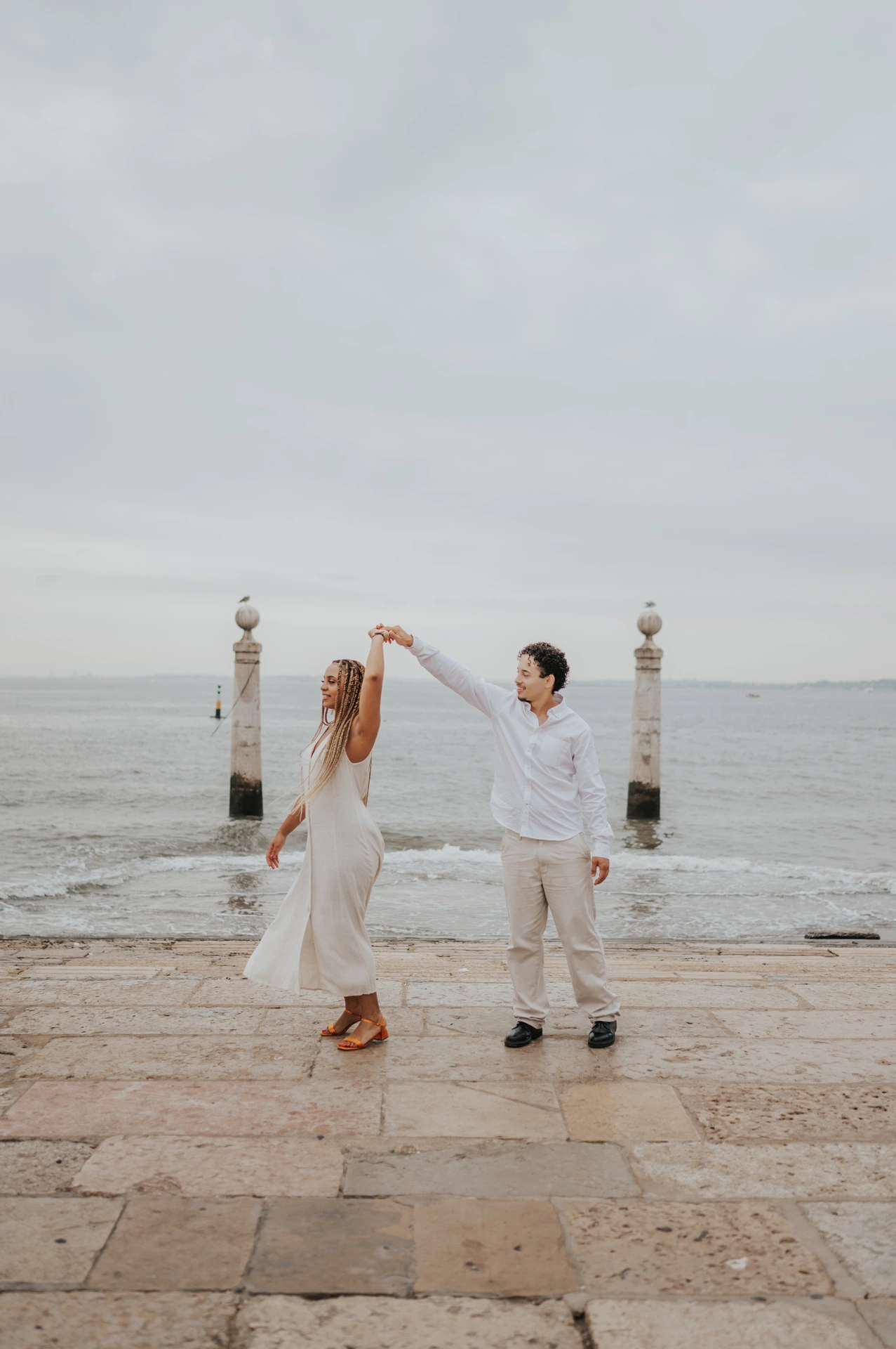 The couple raising their joined hands for a turn on the waterfront steps during their couple photoshoot in Lisbon.