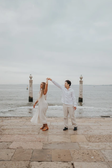 The couple raising their joined hands for a turn on the waterfront steps during their couple photoshoot in Lisbon.
