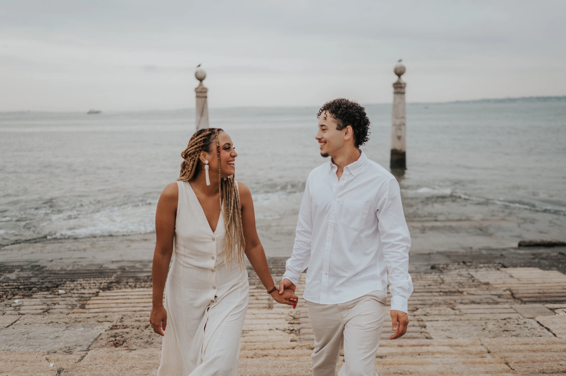 The couple smiling and holding hands as they walk up the stone waterfront steps during their couple photoshoot in Lisbon.