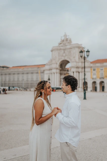 Face to face in the square | Lisbon couple photoshoot The couple facing each other and holding hands with the Praça do Comércio arch behind them during their couple photoshoot in Lisbon.