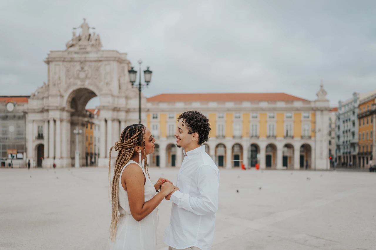 Face to face in the square | Lisbon couple photoshoot The couple facing each other and holding hands with the Praça do Comércio arch behind them during their couple photoshoot in Lisbon.