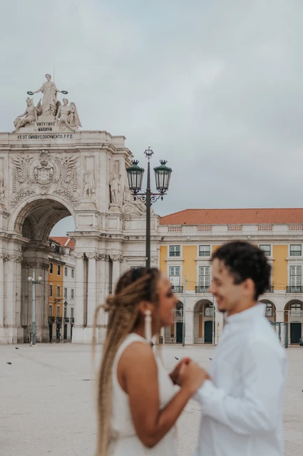 Face to face in the square | Lisbon couple photoshoot The couple facing each other and holding hands with the Praça do Comércio arch behind them during their couple photoshoot in Lisbon.
