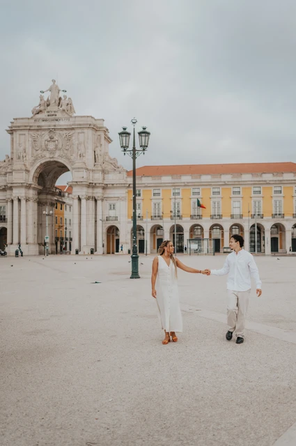 A walk across Praça do Comércio | Lisbon couple photoshoot The couple walking hand in hand across Praça do Comércio with the monumental arch behind them during their couple photoshoot in Lisbon.