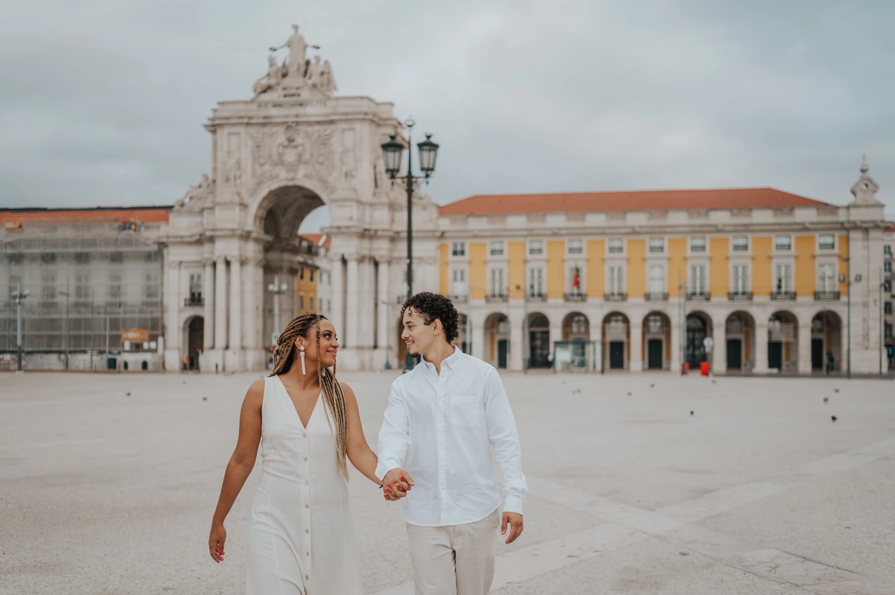 A walk across Praça do Comércio | Lisbon couple photoshoot The couple walking hand in hand across Praça do Comércio with the monumental arch behind them during their couple photoshoot in Lisbon.