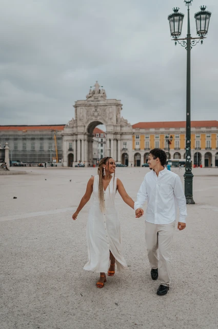A walk across Praça do Comércio | Lisbon couple photoshoot The couple walking hand in hand across Praça do Comércio with the monumental arch behind them during their couple photoshoot in Lisbon.