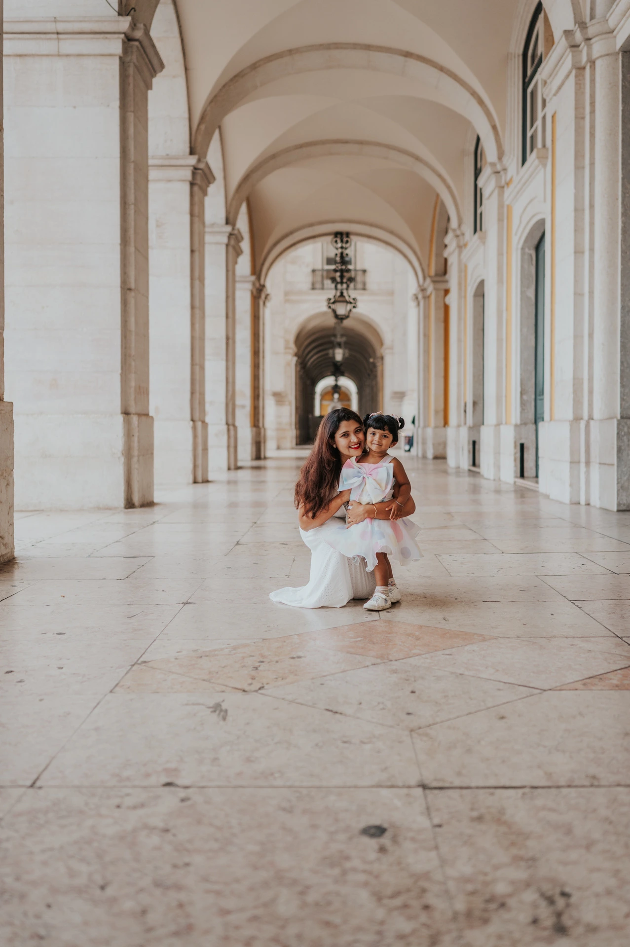 The little girl standing in front of her parents beneath the long stone arcade during their family birthday photoshoot in Lisbon.