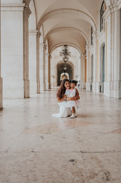 The little girl standing in front of her parents beneath the long stone arcade during their family birthday photoshoot in Lisbon.