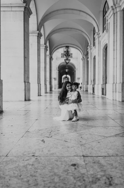 A birthday portrait beneath the arches in black and white | Lisbon family birthday photoshoot Black-and-white photograph: the little girl standing in front of her parents beneath the long stone arcade during their family birthday photoshoot in Lisbon.