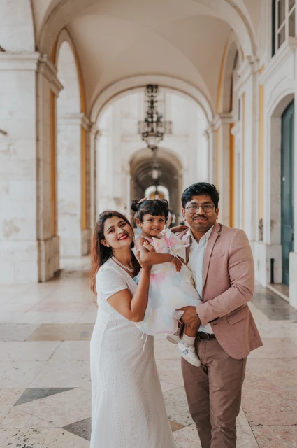 Close together beneath the square’s arcade | Lisbon family birthday photoshoot The parents holding their daughter close beneath the stone arcade at Praça do Comércio during their family birthday photoshoot in Lisbon.