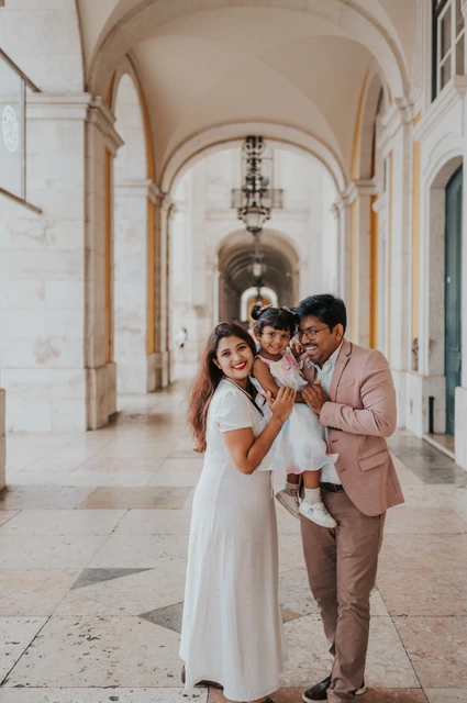 Close together beneath the square’s arcade | Lisbon family birthday photoshoot The parents holding their daughter close beneath the stone arcade at Praça do Comércio during their family birthday photoshoot in Lisbon.