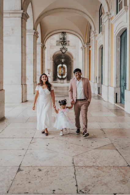 The parents holding their daughter’s hands as they walk together beneath the arcade during their family birthday photoshoot in Lisbon.