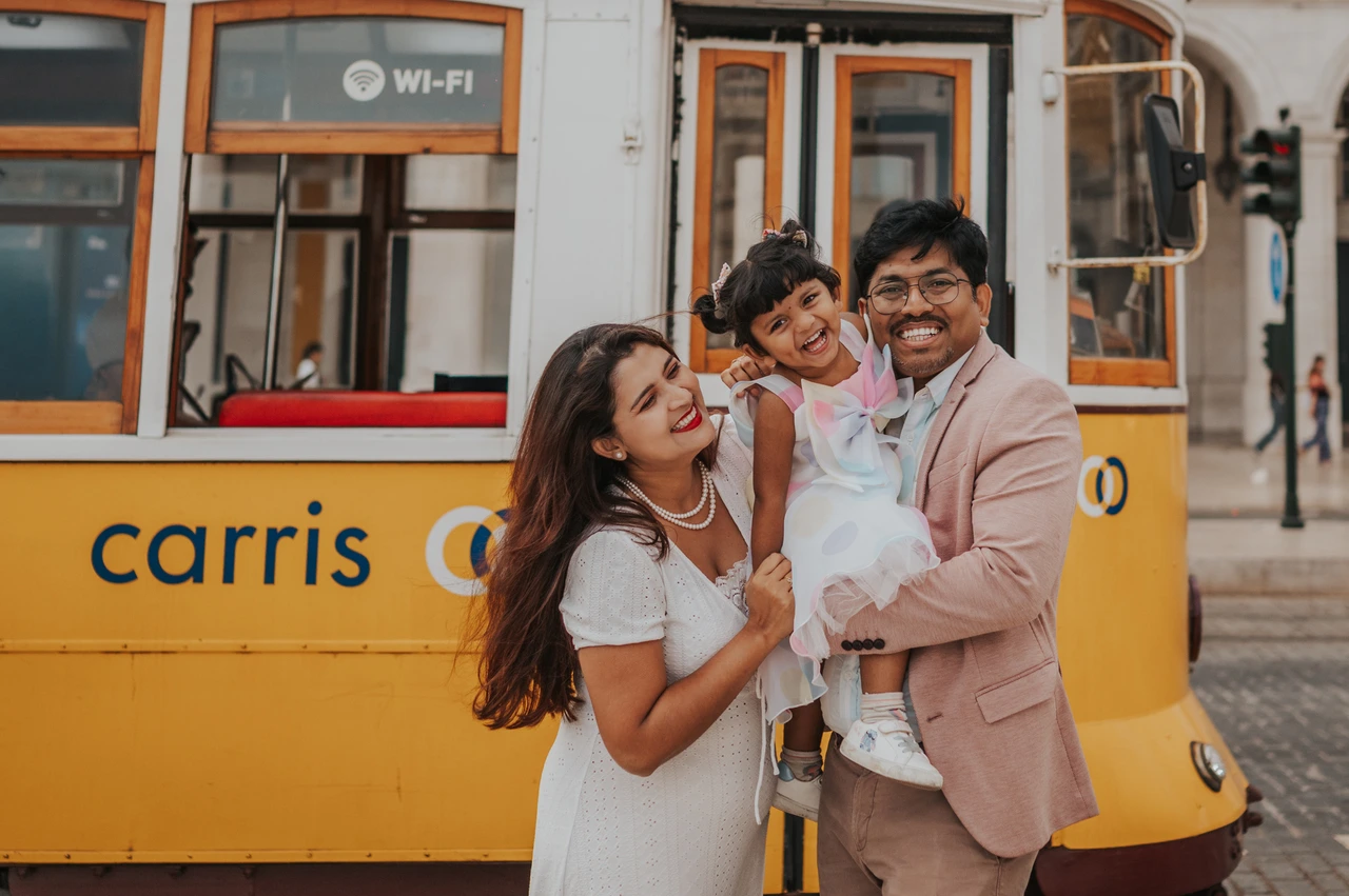A family birthday portrait beside the yellow tram | Lisbon family birthday photoshoot The parents holding their smiling daughter together beside a yellow Lisbon tram during their family birthday photoshoot in Lisbon.