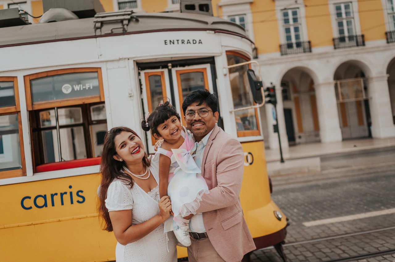 A family birthday portrait beside the yellow tram | Lisbon family birthday photoshoot The parents holding their smiling daughter together beside a yellow Lisbon tram during their family birthday photoshoot in Lisbon.