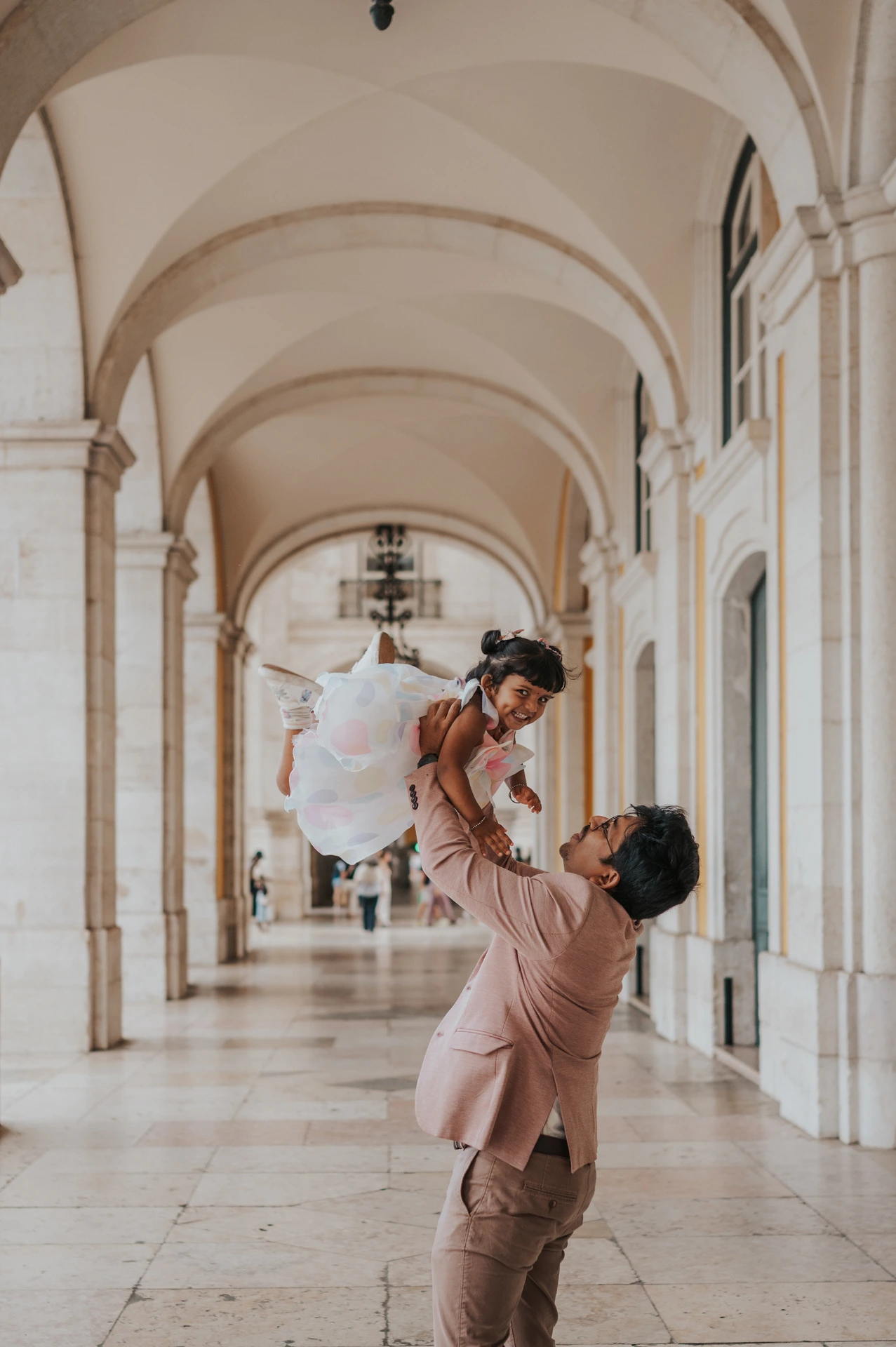 The father lifting his daughter into the air beneath the stone arcade during their family birthday photoshoot in Lisbon.