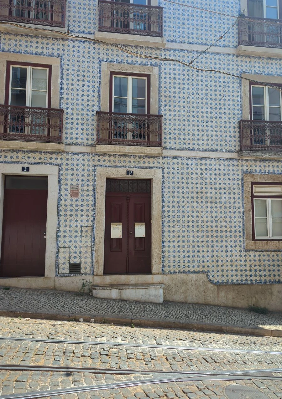 Lisbon Tram Photoshoot - Tiled Street Detail Blue-and-white tiles and iron balconies cover a Lisbon façade beside cobbled tram rails and dark wooden doors.