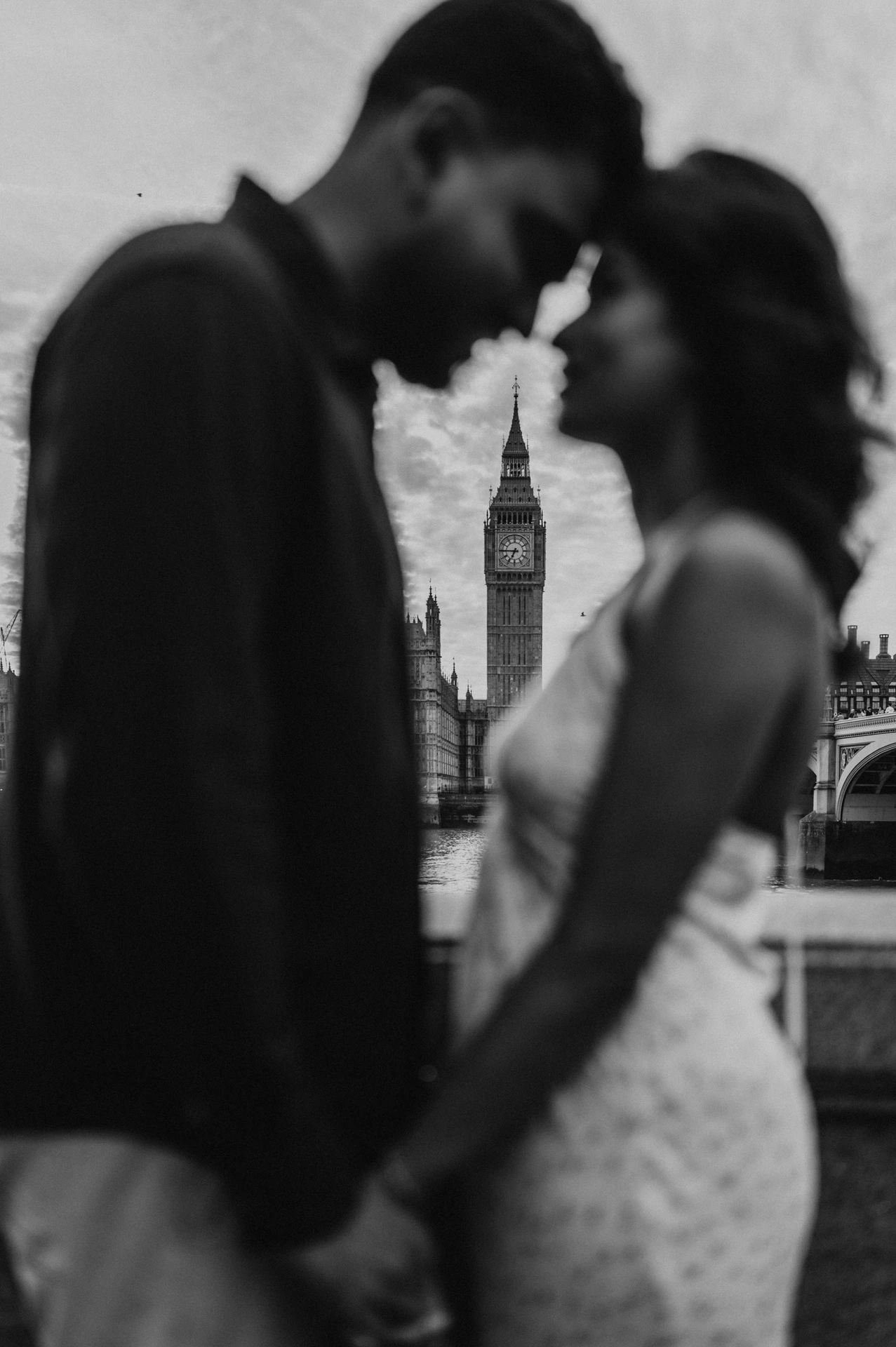 Black-and-white photograph of the softly focused couple touching foreheads, with Big Ben sharp between them, from their London couple photoshoot.