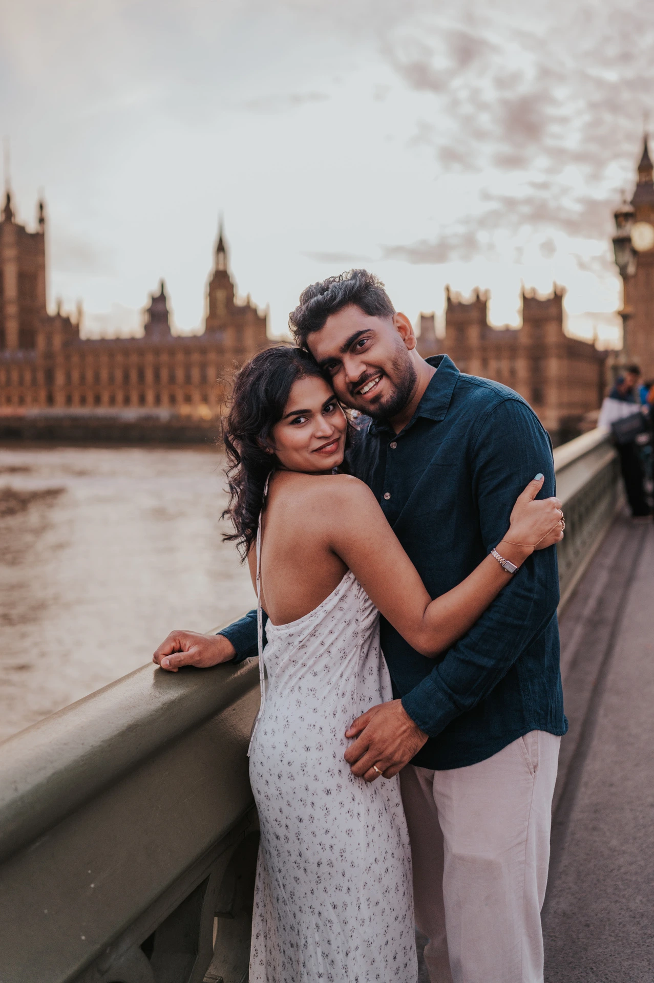 Couple leaning their heads together and smiling at the camera beside the Westminster Bridge parapet during their London couple photoshoot.