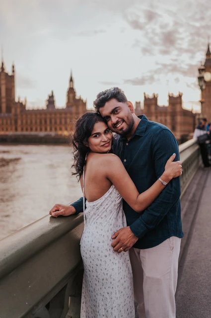 London couple photoshoot smiling on Westminster Bridge Couple leaning their heads together and smiling at the camera beside the Westminster Bridge parapet during their London couple photoshoot.