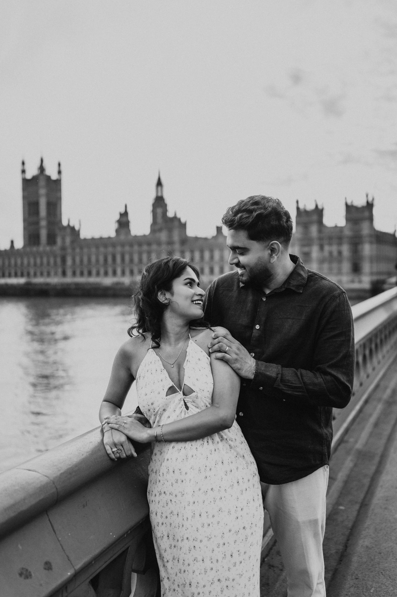 Black-and-white portrait of the couple looking at each other beside the Westminster Bridge parapet, from their London couple photoshoot.