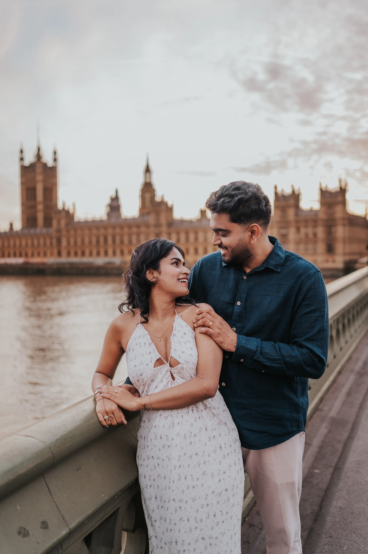 Couple looking at each other beside the Westminster Bridge parapet, with the Houses of Parliament across the Thames, during their London couple photoshoot.