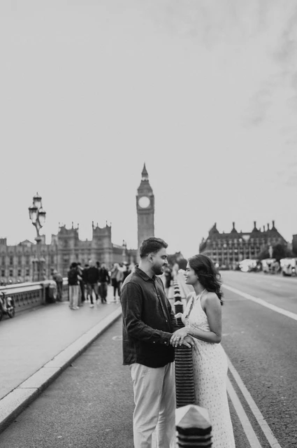 Black-and-white portrait of the couple standing together beside the roadway on Westminster Bridge, with Big Ben behind, from their London couple photoshoot.