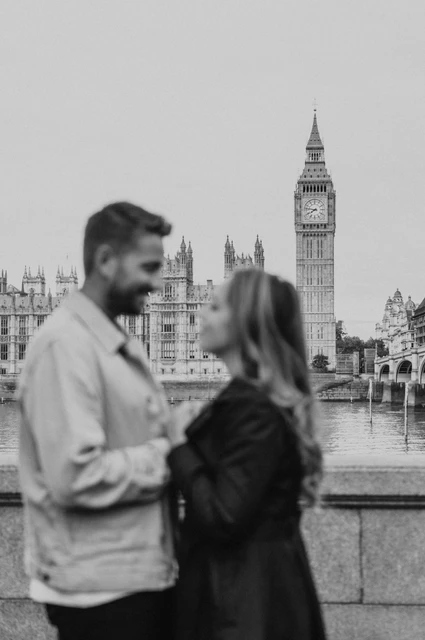 London couple photoshoot in black and white with Big Ben Black-and-white photograph of a softly focused couple in the foreground, with Big Ben across the Thames, during their London photoshoot.