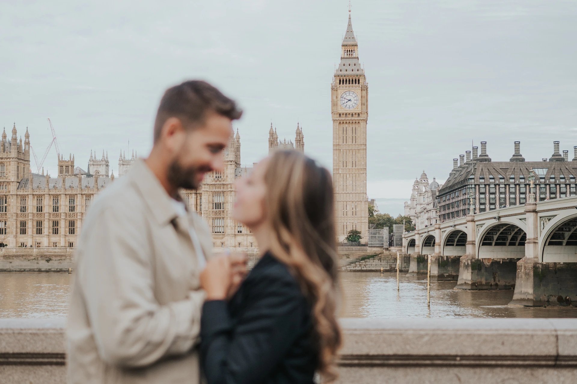 London couple photoshoot with Big Ben in focus across the Thames Landscape photograph with the couple softly focused in front of Big Ben, Parliament and Westminster Bridge during their London couple photoshoot.