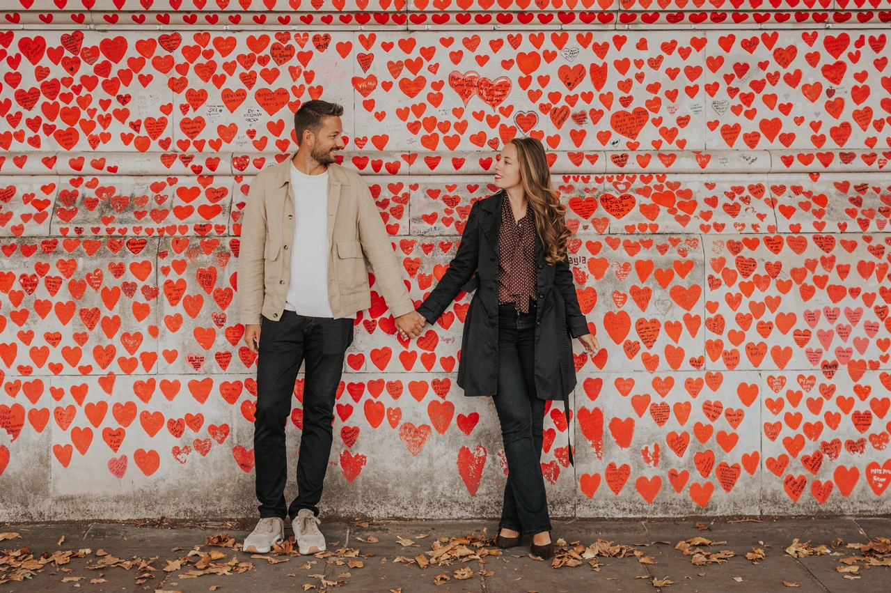 London couple photoshoot beside the National Covid Memorial Wall Couple holding hands beside the red hearts of the National Covid Memorial Wall during their London couple photoshoot.