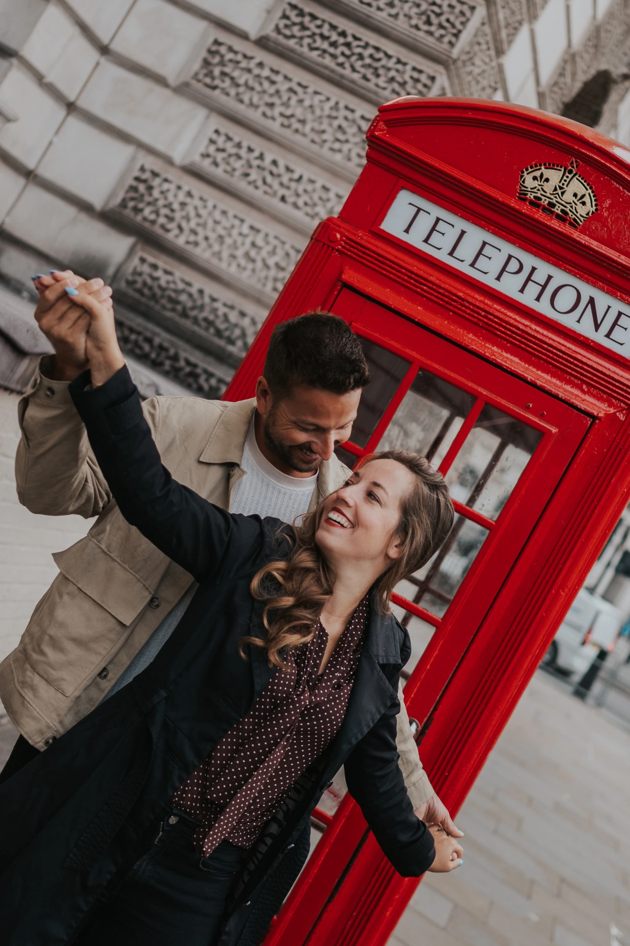 London couple photoshoot beside a red telephone box Smiling couple with their joined hands raised beside a bright red telephone box during their London couple photoshoot.