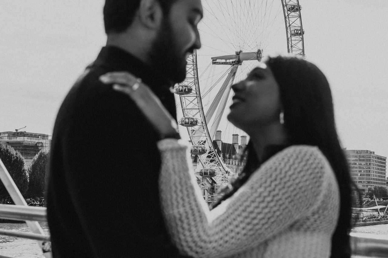 A close bridge embrace in black and white — London couple photoshoot A close black-and-white portrait of the couple embracing beside the Golden Jubilee Bridge railing, with the London Eye in the background during their London couple photoshoot.