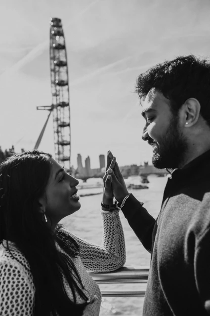 A black-and-white close portrait of the couple touching their raised palms on Golden Jubilee Bridge, with the London Eye behind them during their London couple photoshoot.