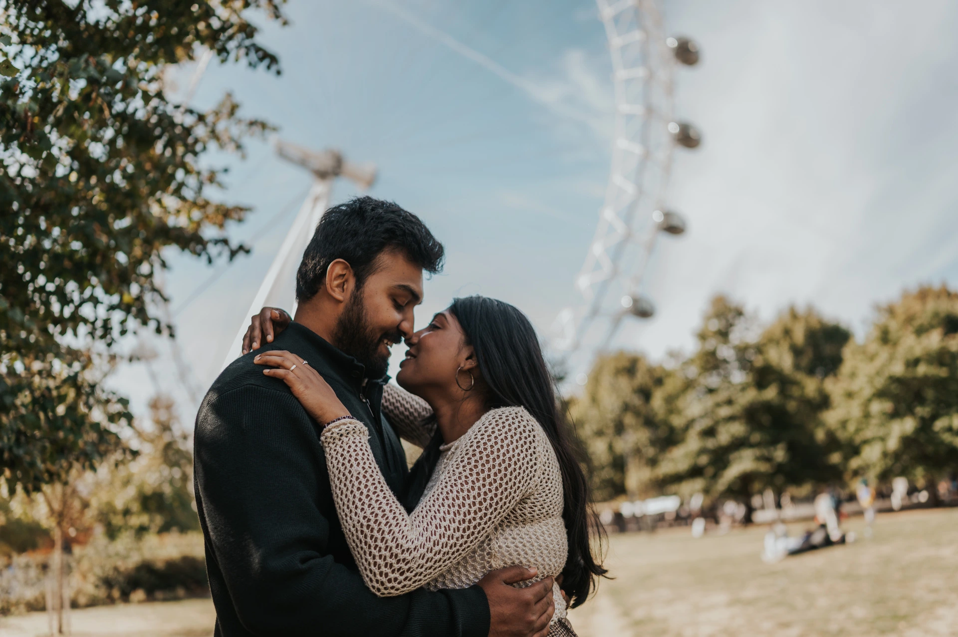 A close portrait of the couple leaning towards a kiss in Jubilee Gardens, with her hands at his shoulders and the London Eye behind them during their London couple photoshoot.