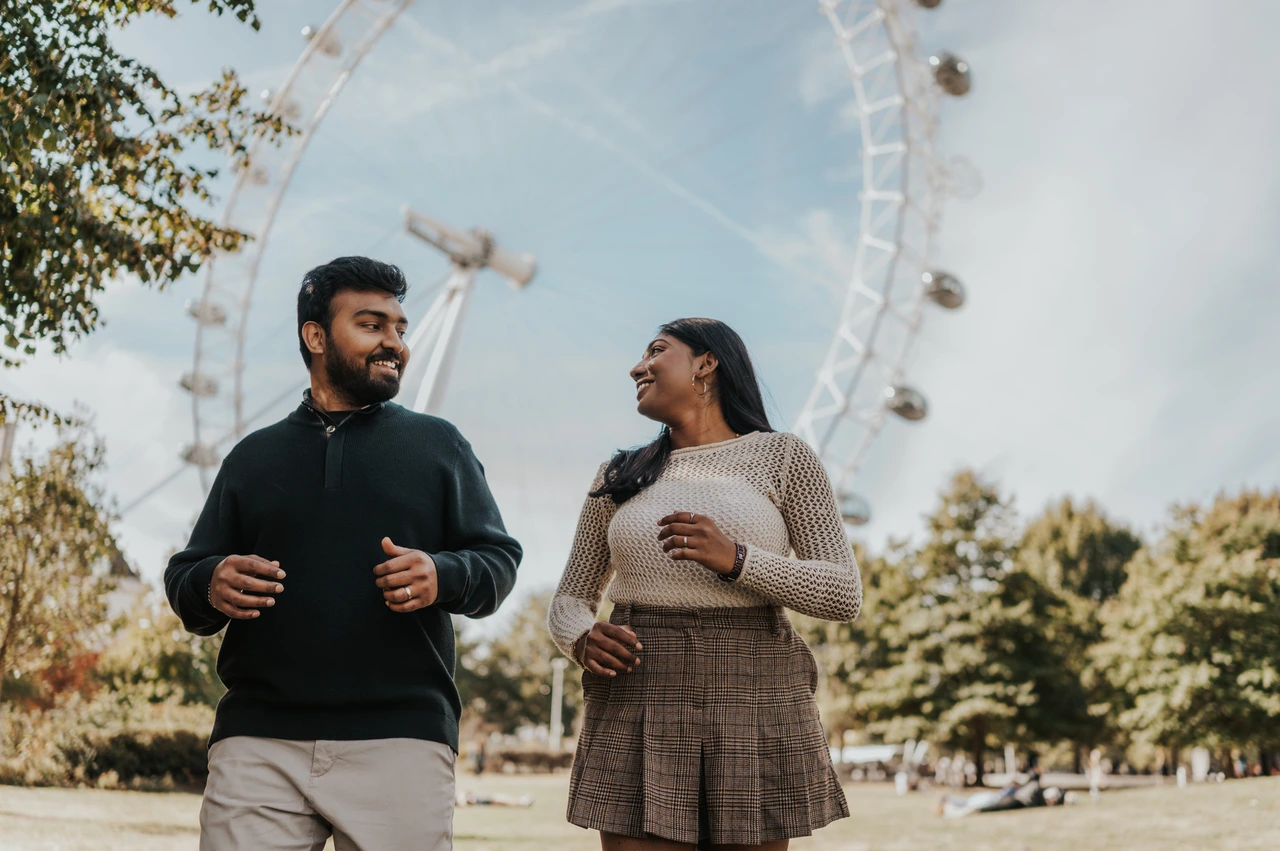 A closer couple portrait on the Jubilee Gardens lawn — London couple photoshoot The couple looking at one another in a closer landscape portrait on the Jubilee Gardens lawn, with the London Eye and leafy trees behind them during their London couple photoshoot.
