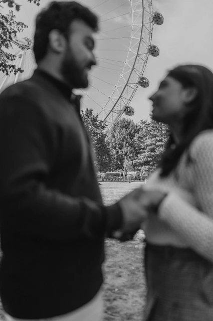 A soft-focus portrait beneath the wheel in black and white — London couple photoshoot A black-and-white photograph of the softly focused couple facing each other in Jubilee Gardens, with the London Eye visible above them during their London couple photoshoot.