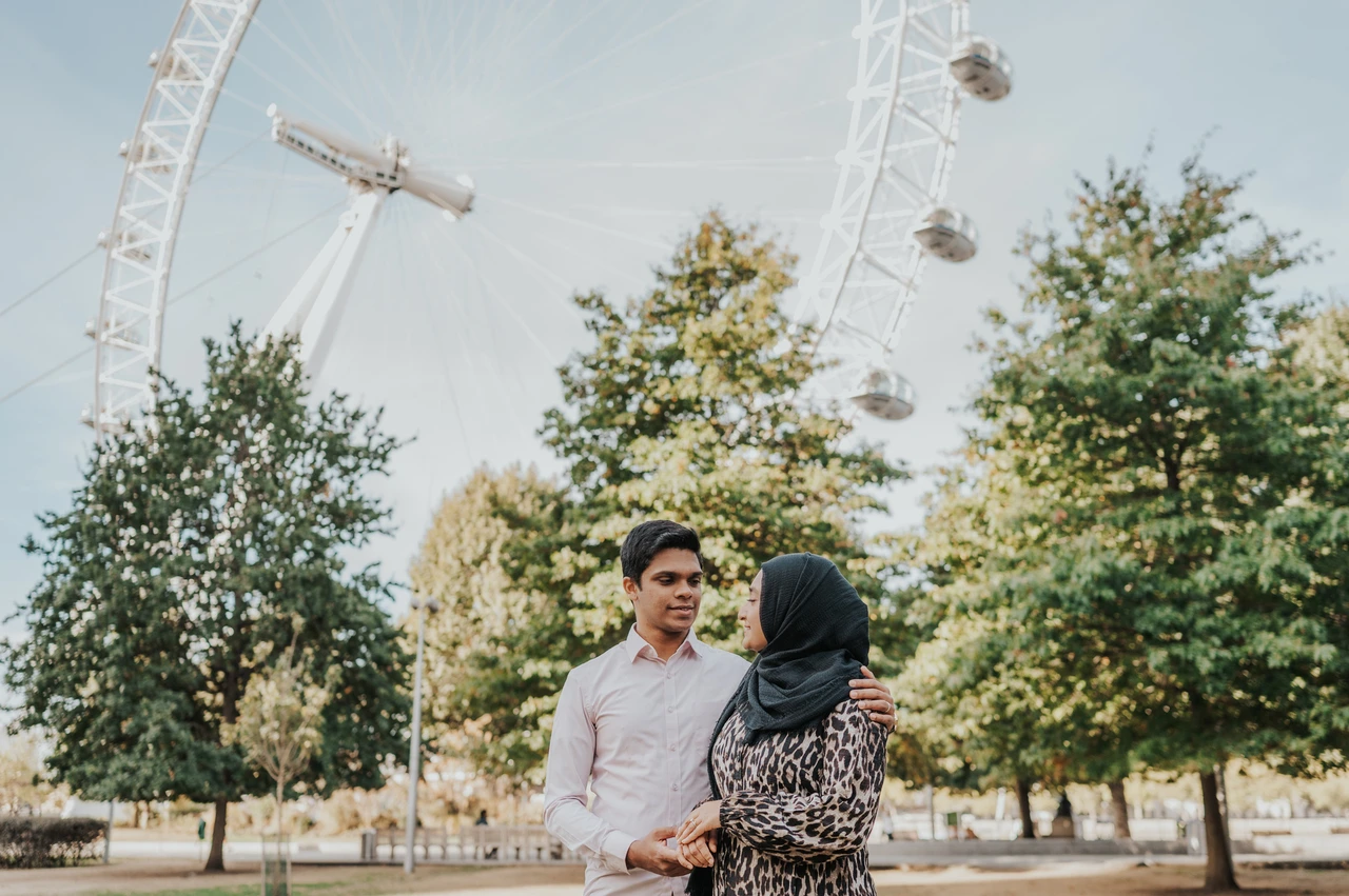 London couple photoshoot together beneath the London Eye Couple standing close together beside the trees in Jubilee Gardens, beneath the London Eye, during their London photoshoot.
