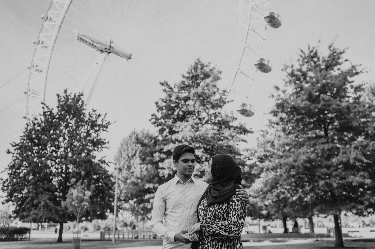 Black-and-white London couple photoshoot in the gardens Black-and-white portrait of the couple standing close together in Jubilee Gardens with the London Eye above the trees, from their London photoshoot.