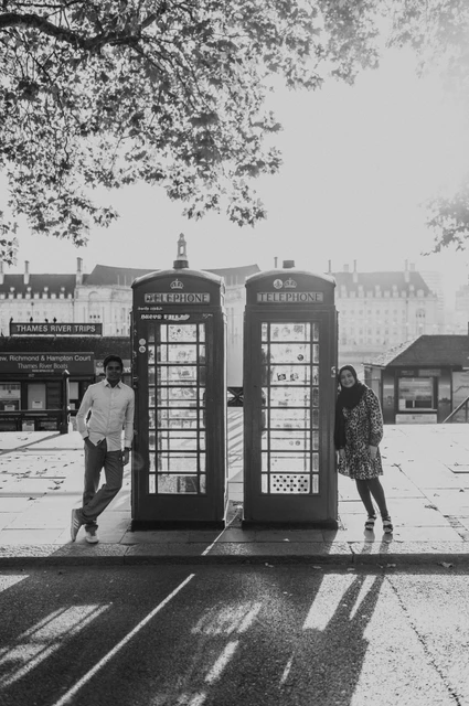 Black-and-white photograph of the couple standing on either side of a telephone box near Westminster Pier, with Big Ben behind them, from their London photoshoot.