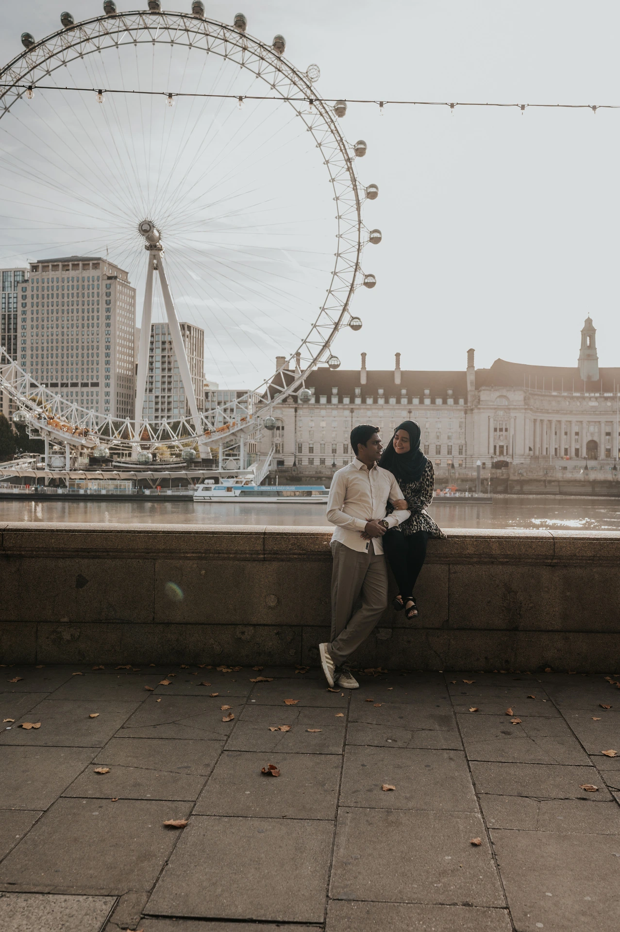 Couple together by the Thames at Westminster Pier, framed beneath the London Eye and riverside lights, during their London photoshoot.