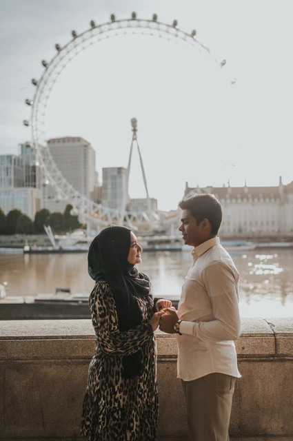 Close London couple photoshoot with the London Eye backdrop Close portrait of the couple holding hands by the Thames, with the London Eye above the riverside wall, during their London photoshoot.