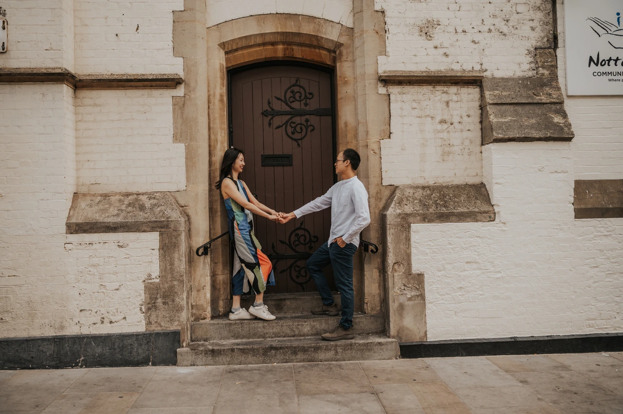 London couple photoshoot: a wide portrait beneath an arched doorway A wide view of the couple holding hands on the steps beneath an arched wooden doorway during their London couple photoshoot.