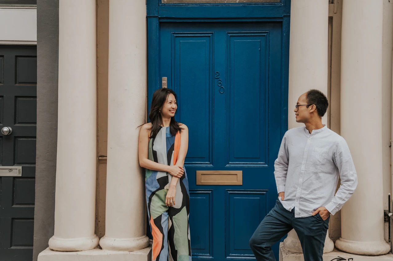 London couple photoshoot: facing each other beside a bright blue doorway A wide portrait of the couple facing each other beside a bright blue front door framed by cream columns during their London couple photoshoot.