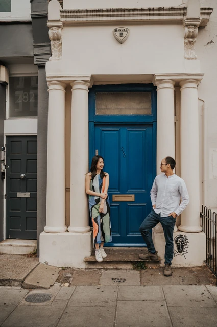 London couple photoshoot: a relaxed portrait at the blue front door A full-height portrait of the couple standing on either side of a bright blue front door in Notting Hill during their London couple photoshoot.