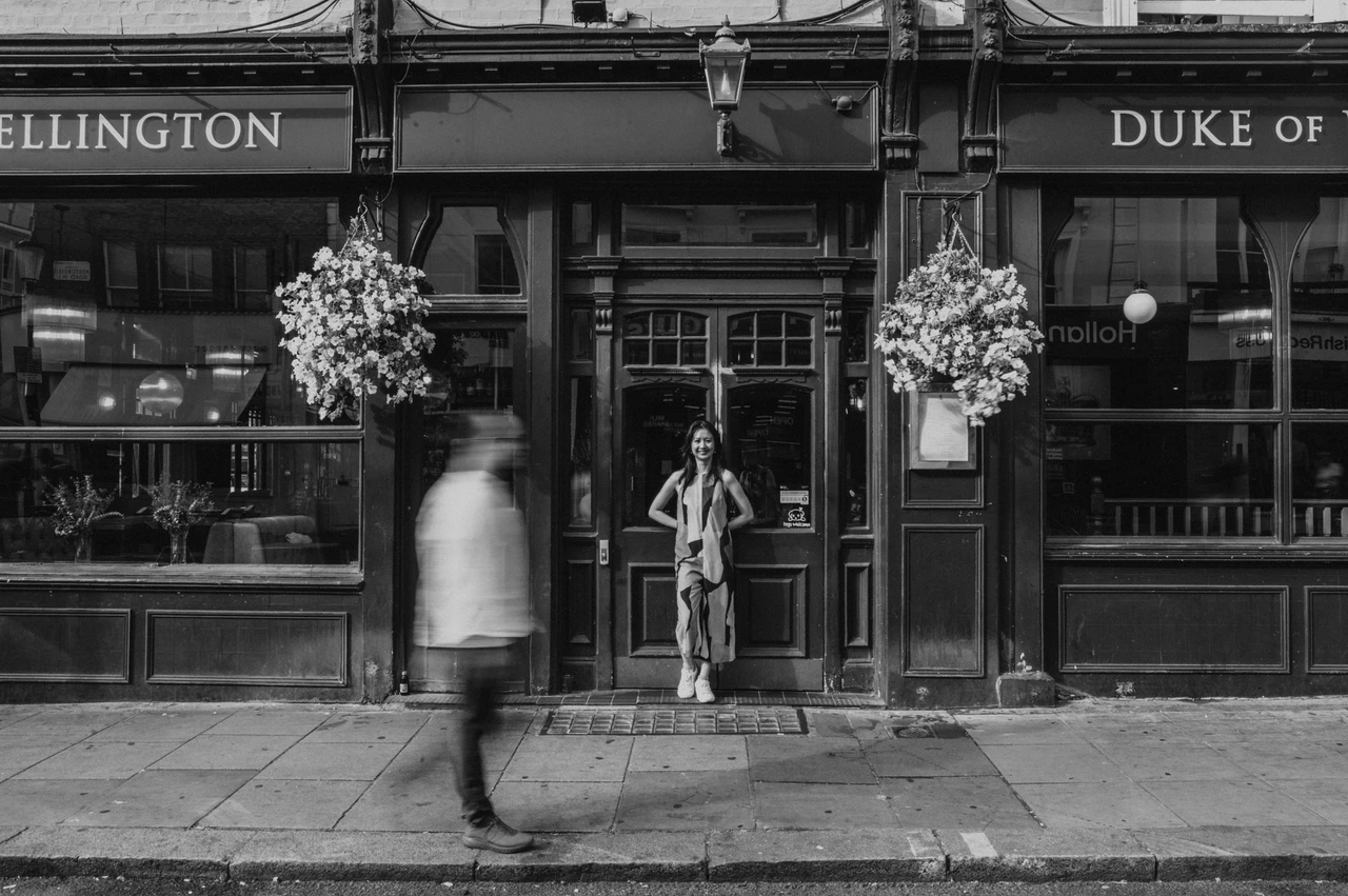 London couple photoshoot: outside the Duke of Wellington in black and white A black-and-white view of the couple outside the Duke of Wellington pub with a blurred pedestrian passing in the foreground during their London couple photoshoot.