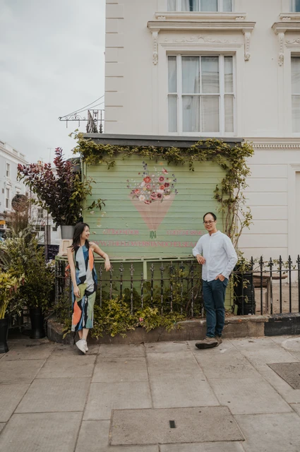 London couple photoshoot: smiling beside a painted floral shutter The couple stand apart and smile beside a green shop shutter painted with a bouquet of flowers during their London couple photoshoot.