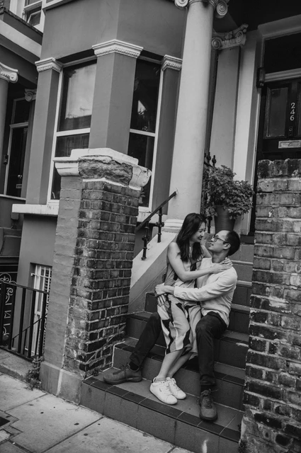 London couple photoshoot: a seated embrace on Notting Hill steps in black and white A black-and-white view of the couple leaning close together while seated on the front steps in Notting Hill during their London couple photoshoot.