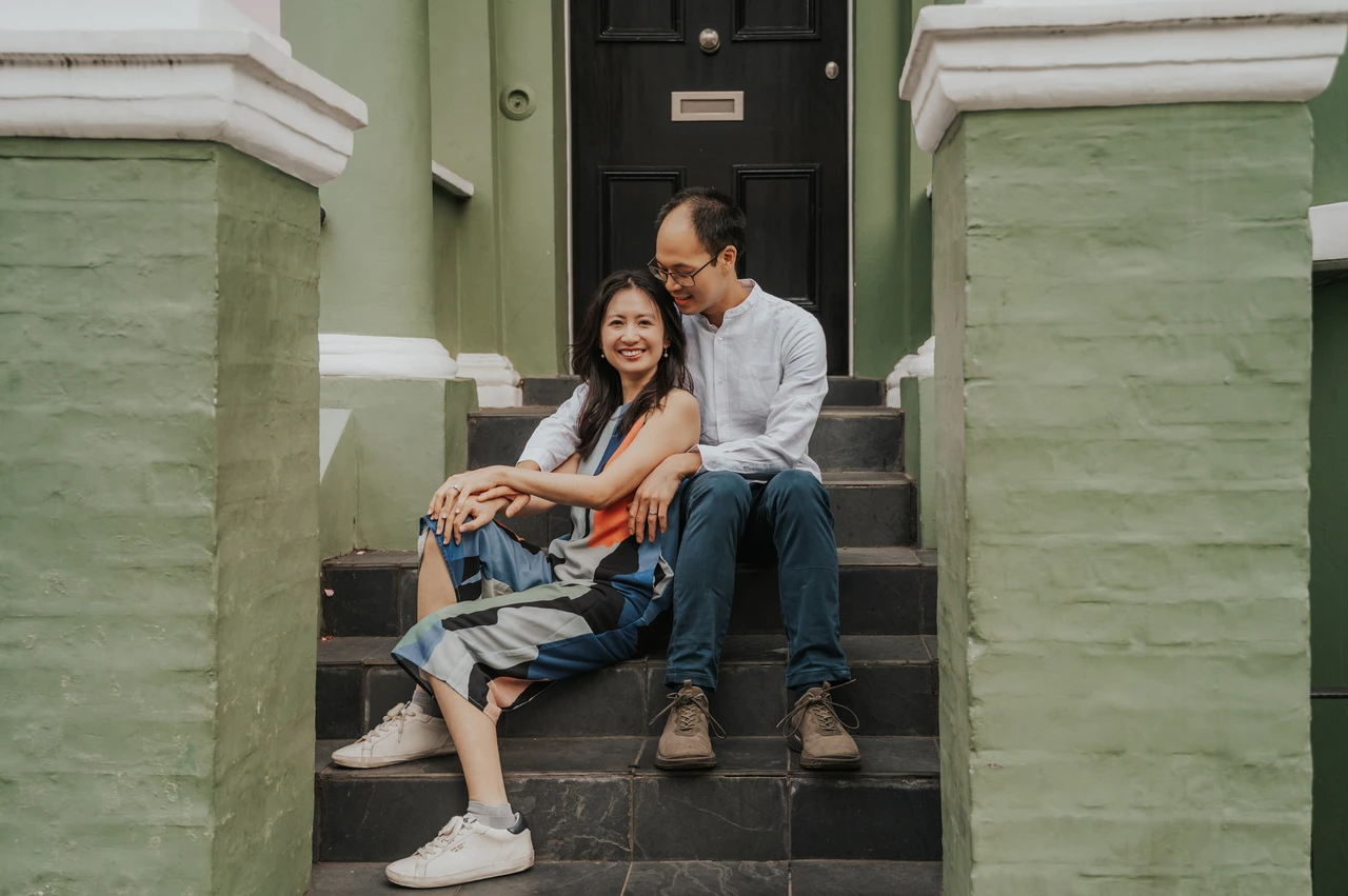 London couple photoshoot: a wide portrait on the green house staircase A wide view of the couple sitting together on the steps between the green house walls and brick gateposts during their London couple photoshoot.