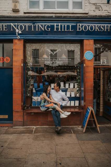 She sits on his lap on the bench outside The Notting Hill Bookshop as they look towards each other during their London couple photoshoot.