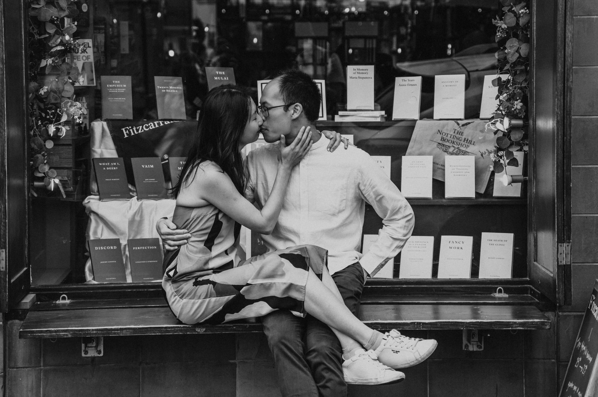 A black-and-white close portrait of the couple kissing on the bench outside The Notting Hill Bookshop during their London couple photoshoot.