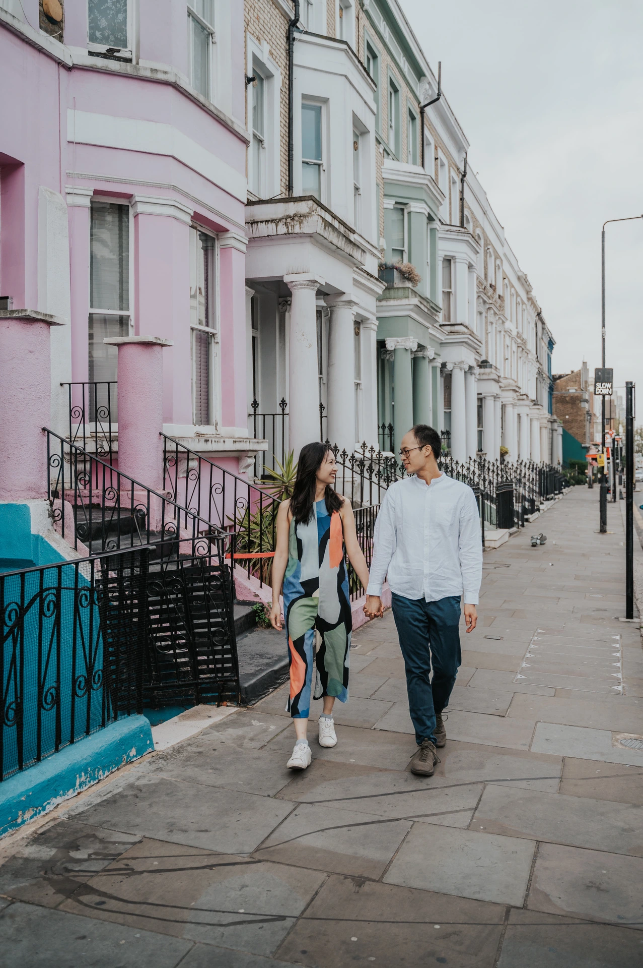 The couple walk hand in hand beside pastel pink, green and white terraced houses in Notting Hill during their London couple photoshoot.